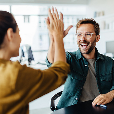 Mann und Frau in einem Büro geben sich ein High-Five.