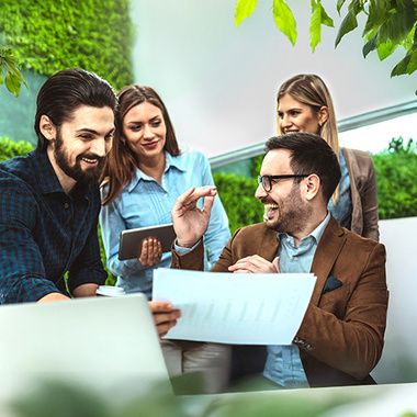 Eine Gruppe von Mitarbeitenden sitzt gemeinsam an einem Tisch und diskutiert ein Projekt